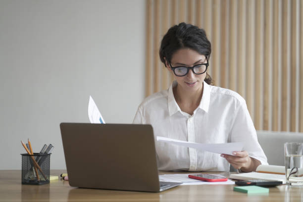 A businesswoman reviews documents at a desk with a laptop, illustrating decision-making for business locations in Dubai.