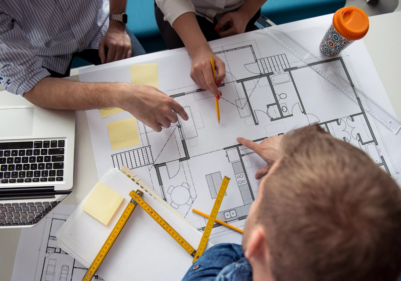 Three people discussing architectural plans spread out on a table.