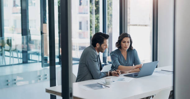 Two business professionals collaborate over a laptop in a modern office, discussing joint ventures in Dubai.